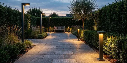 Moderne Wegeleuchten beleuchten einen gepflasterten Gartenweg bei Nacht - Symbolbild KI-generiert