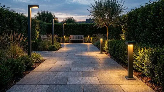 Moderne Wegeleuchten beleuchten einen gepflasterten Gartenweg bei Nacht